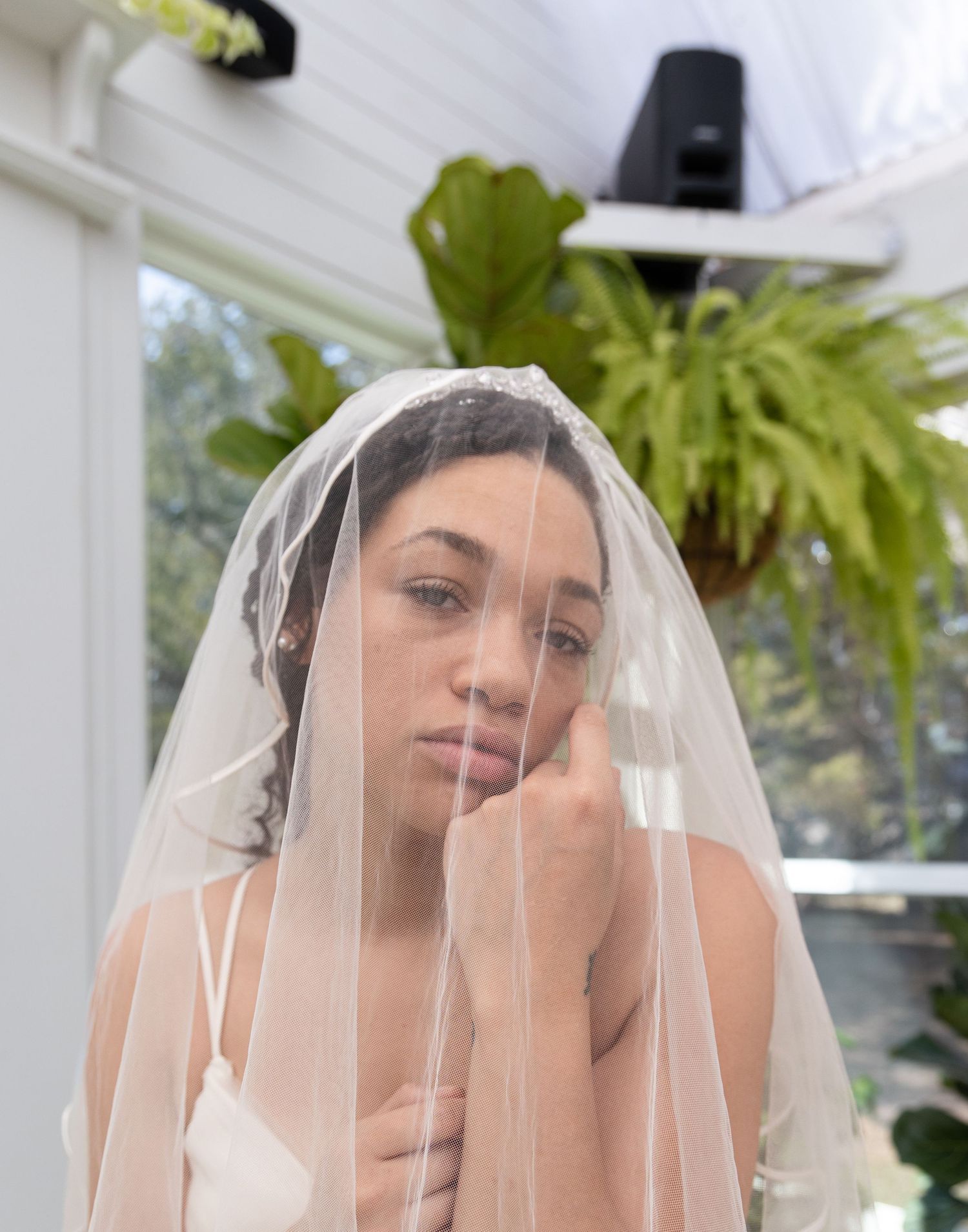 Close-up portrait of a bride wearing a sheer veil in a sunlit indoor setting.