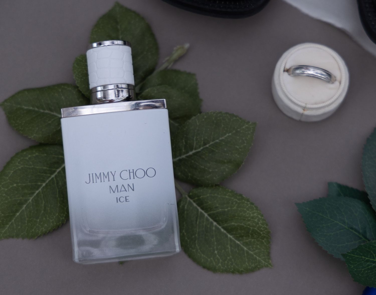 A Jimmy Choo fragrance bottle arranged with green leaves and wedding rings.