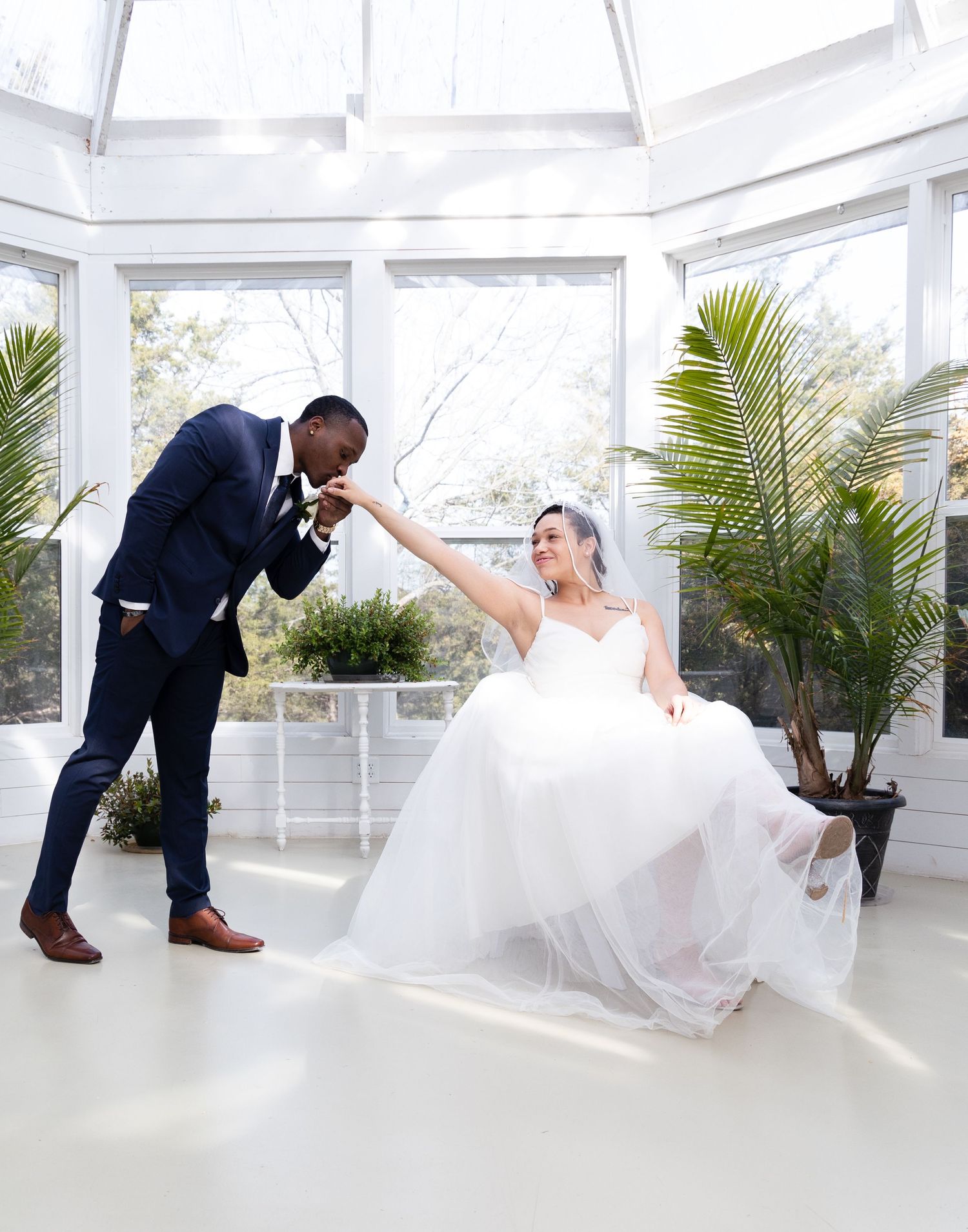 Playful wedding photo in a bright conservatory with tropical plants.