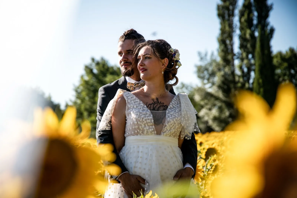 Jeune couple de mariés souriant dans un champ de tournesols, journée ensoleillée et joyeuse.