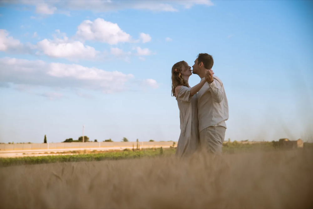 Demande en mariage en pleine nature, le couple s’enlaçant dans un champ sous un ciel bleu.
