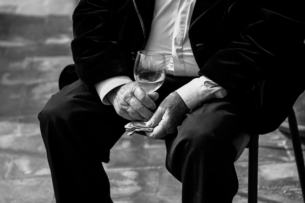 Portrait en noir et blanc d’un homme assis, vêtu d’un costume, les mains croisées posées sur une canne.