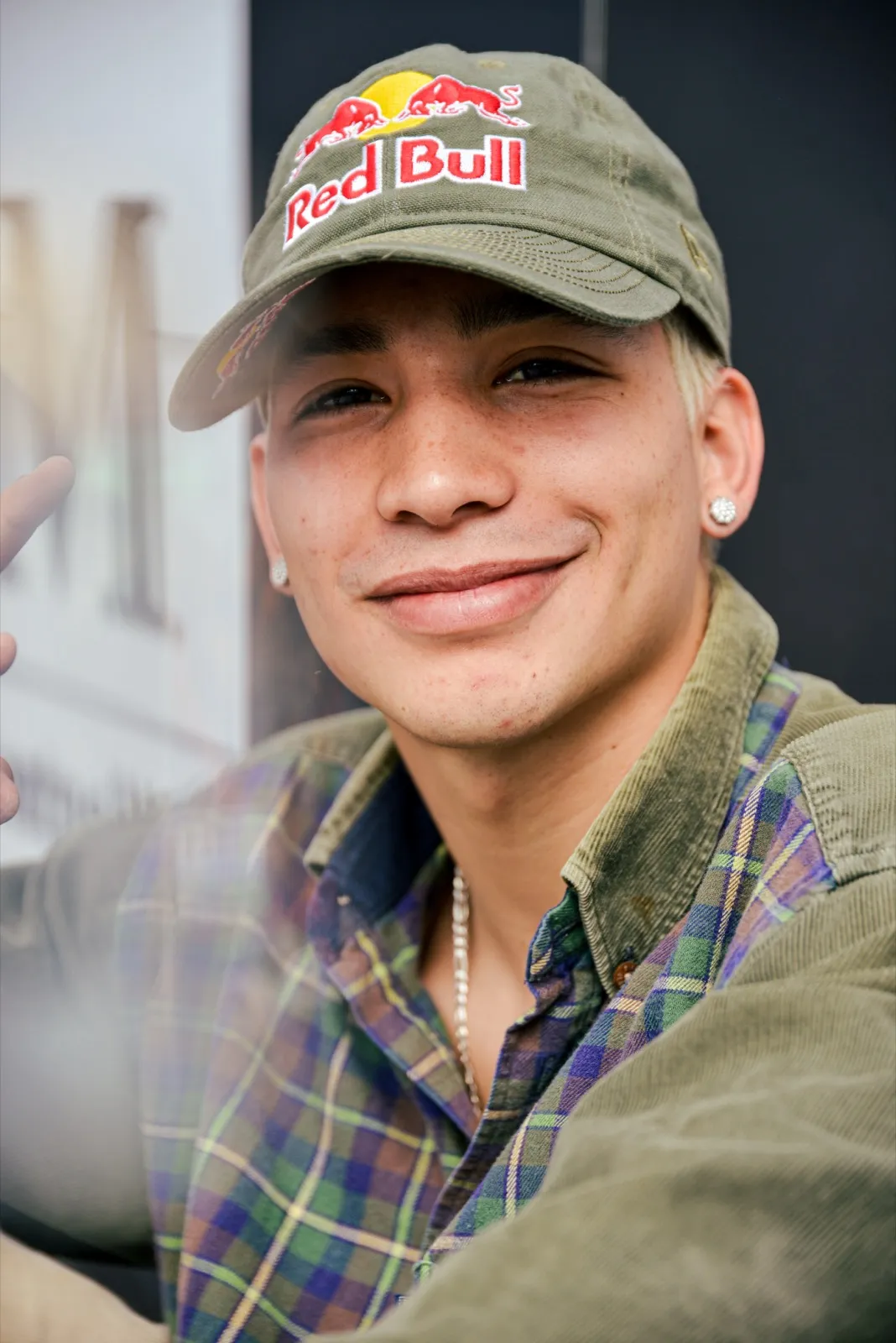 Portrait d’un athlète Red Bull souriant, vêtu d’une chemise à carreaux et casquette verte, dans une ambiance chaleureuse.