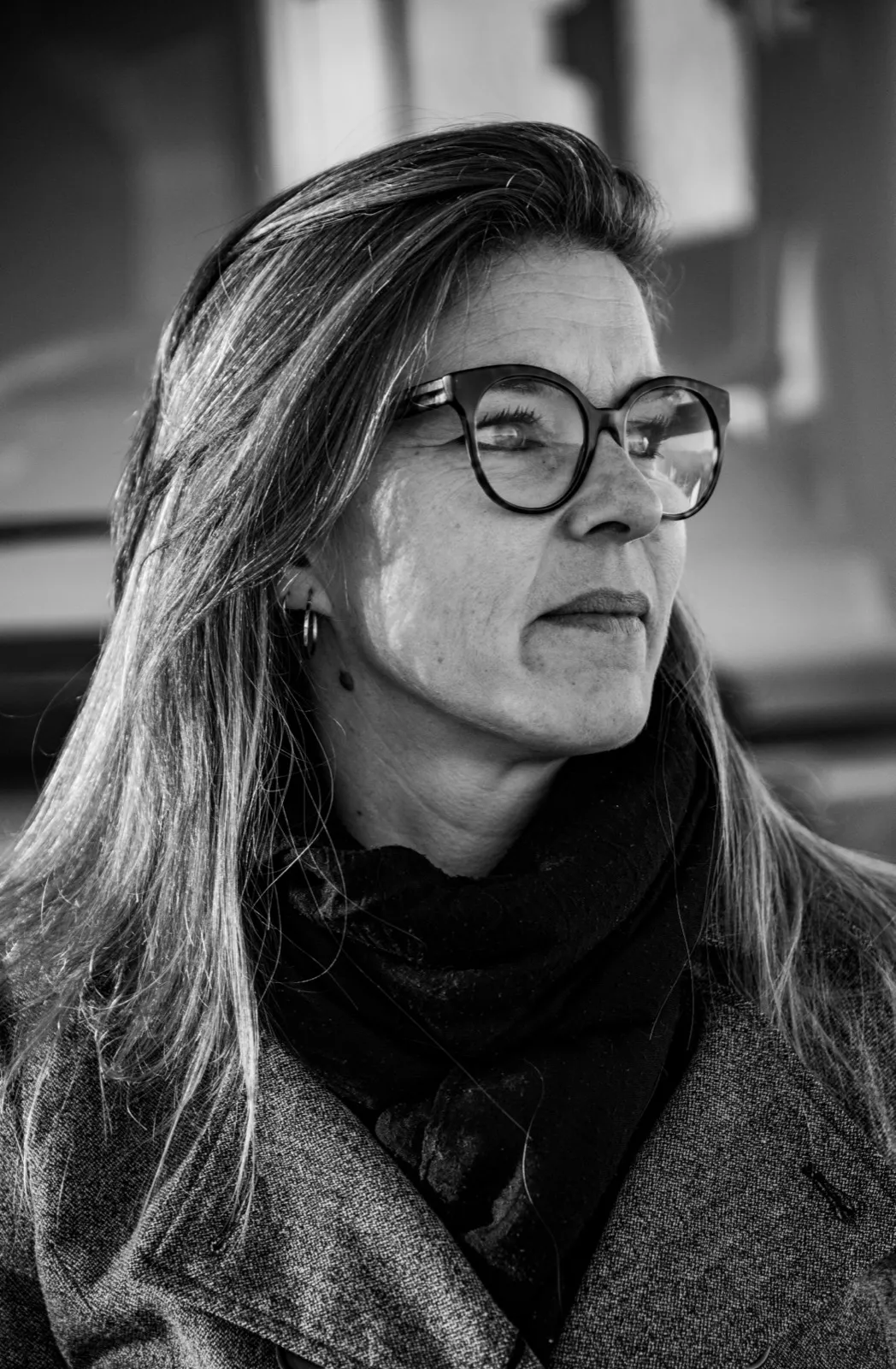 Portrait en noir et blanc d’une femme portant des lunettes, écharpe et manteau, regardant sur le côté
