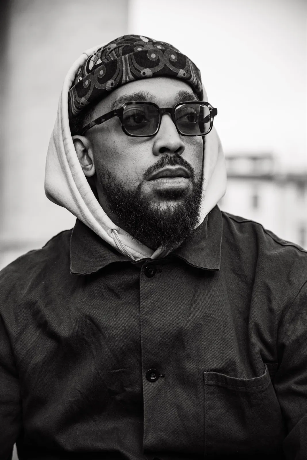 Portrait en noir et blanc d’un homme portant un sweat à capuche et des lunettes de soleil, expression sérieuse.