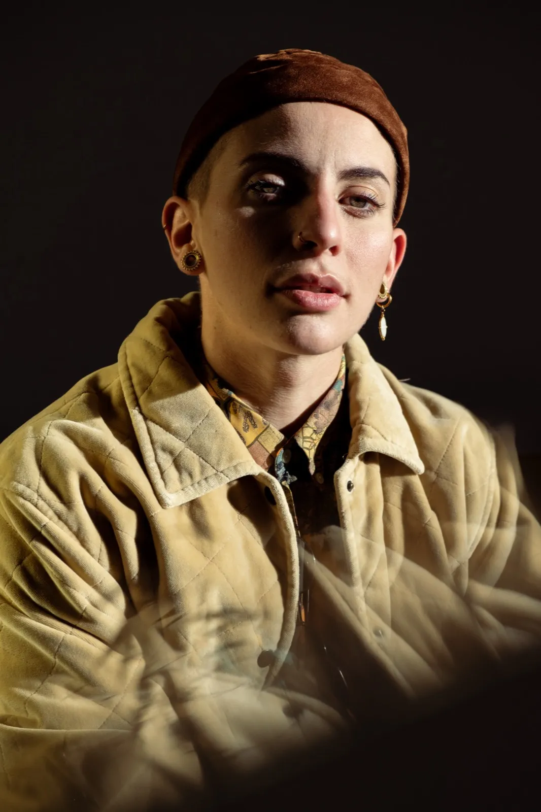 Portrait studio d’une femme en chemise beige, regard sérieux, éclairage tamisé.