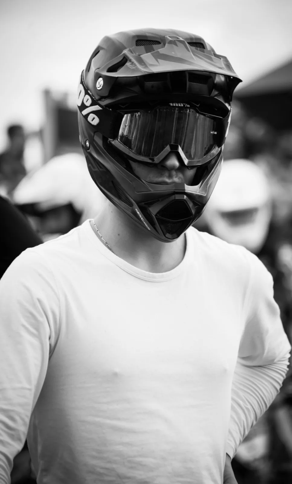 Portrait d’un rider en t-shirt clair portant un casque intégral, debout dans un environnement sportif.