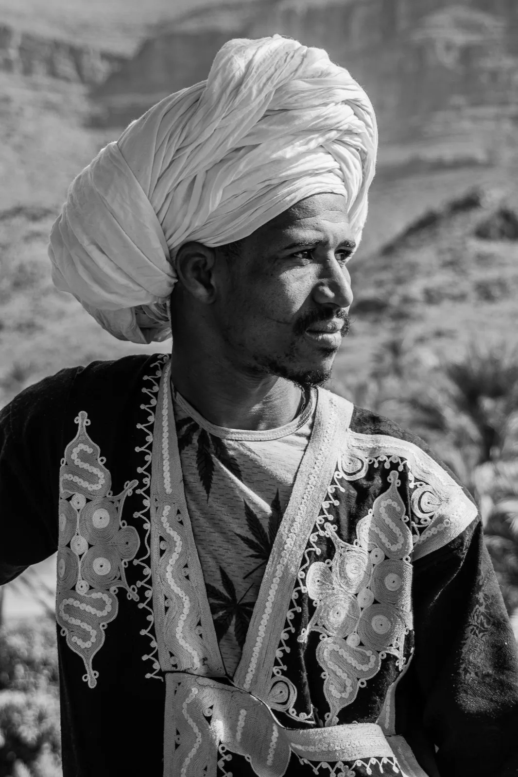Portrait en noir et blanc d’un homme en habits traditionnels et turban, capturé en extérieur.