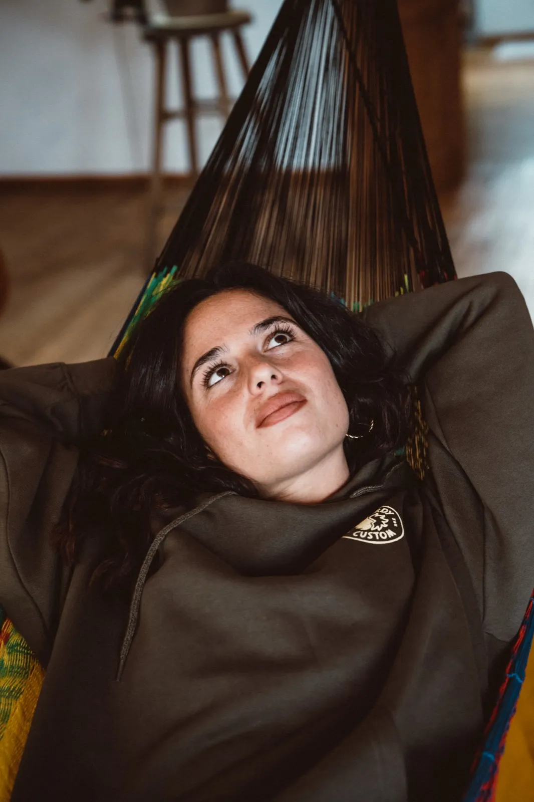 Jeune femme allongée dans un hamac à l’intérieur, regard rêveur tourné vers le haut.