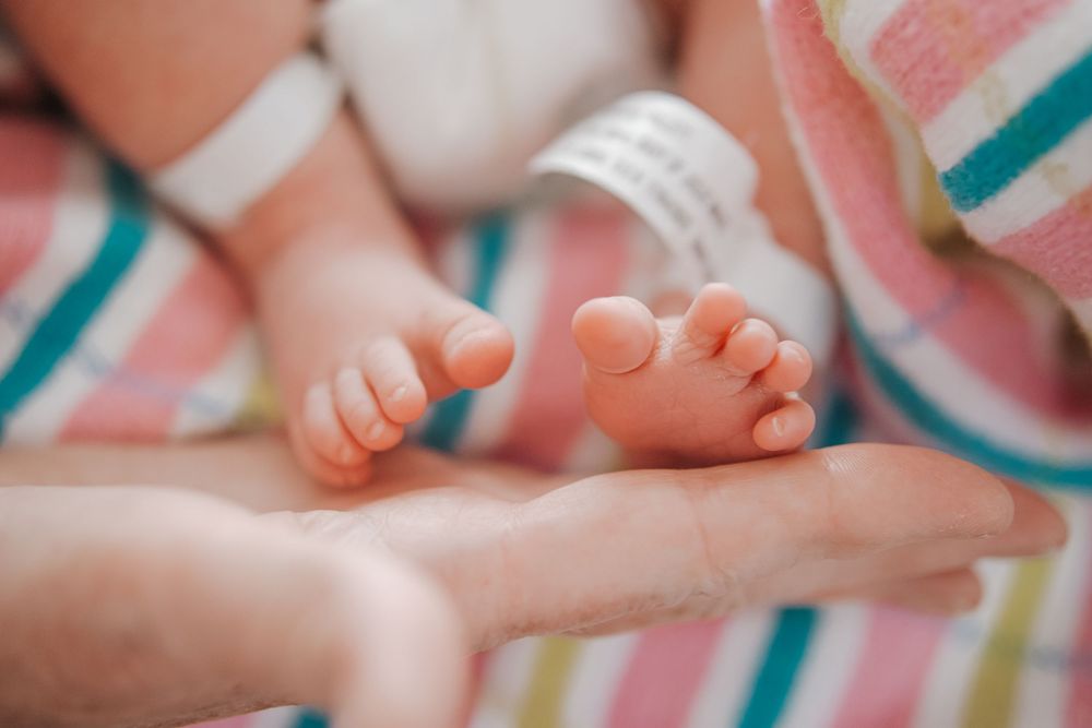 Close-up photo of tiny baby feet resting on colorful striped blanket with soft focus background.