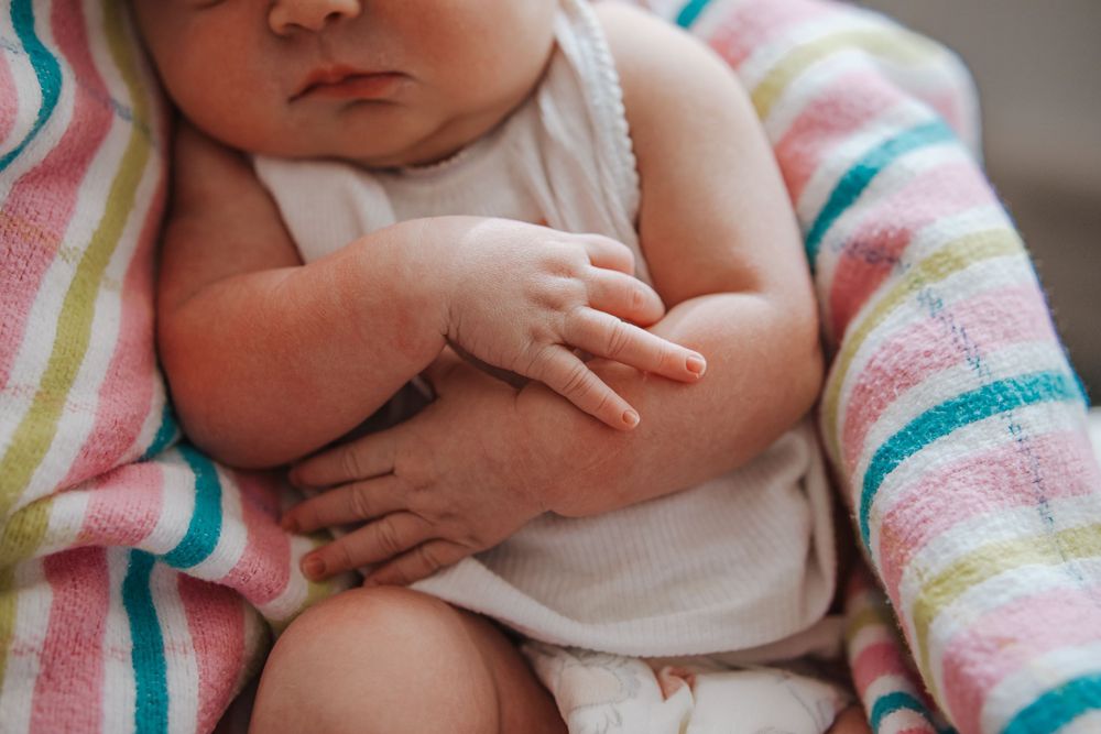 Close up view of baby hands and torso wrapped in a colorful striped blanket.