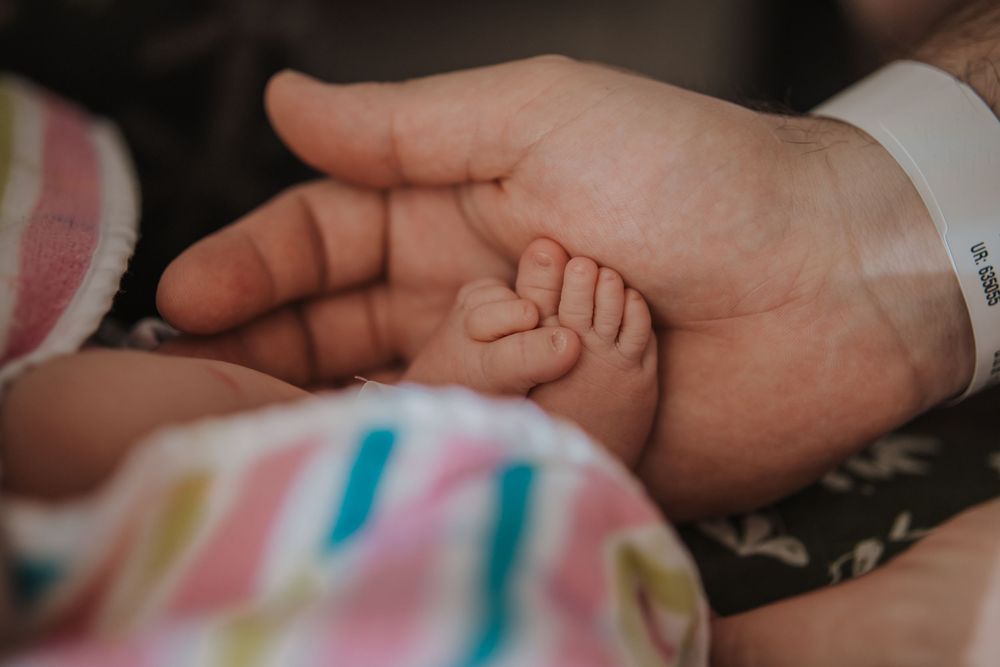 A tiny baby hand gently rests in an adult's palm against a striped textile background.
