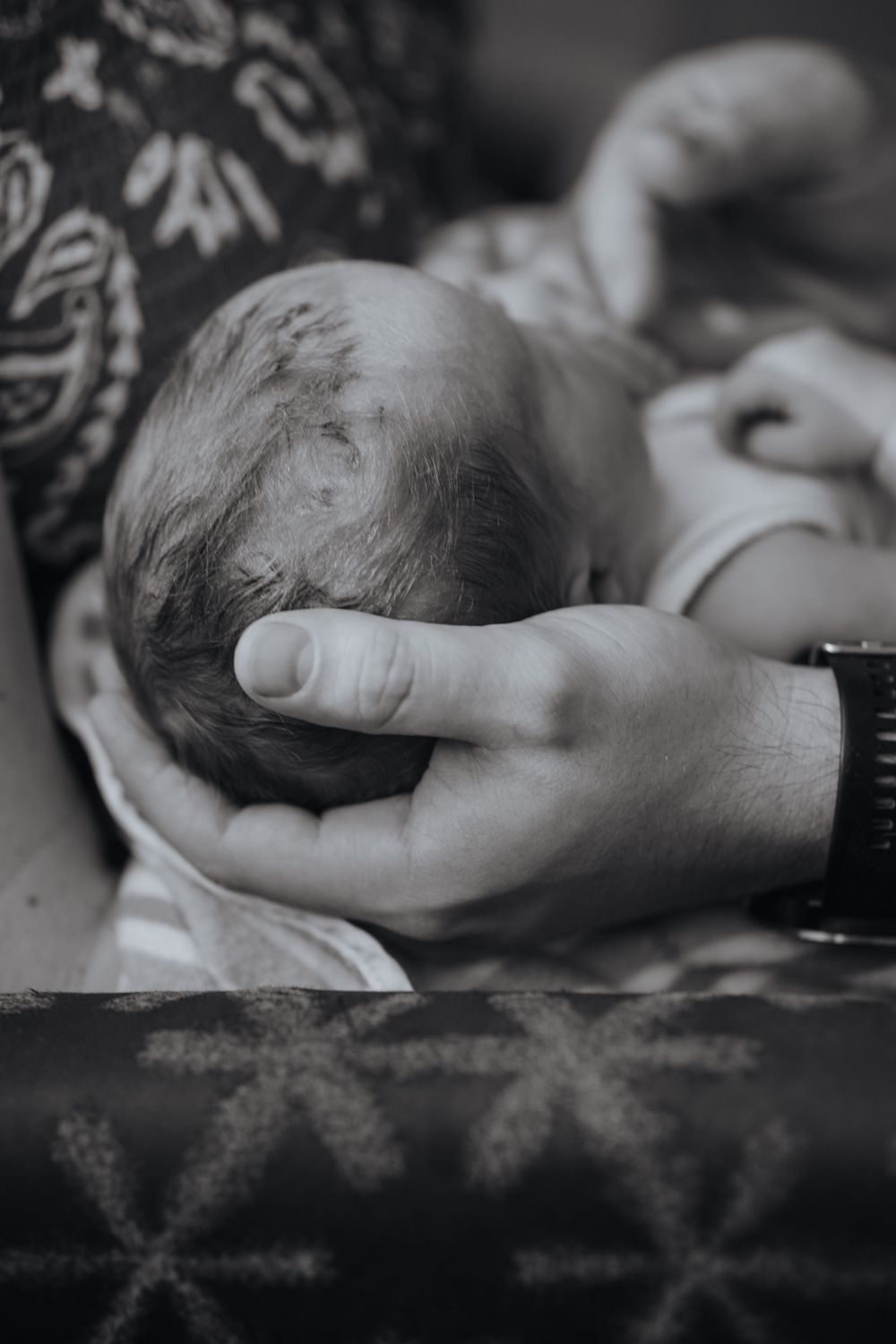 A tender black and white shot of gentle hands cradling a newborn baby's head.