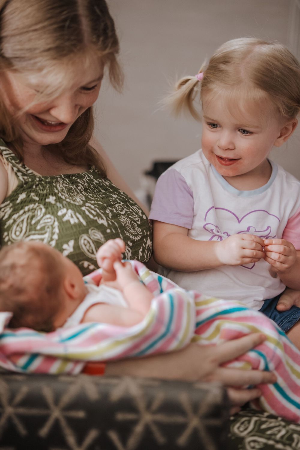 A joyful family moment as siblings gather around a newborn swaddled in a striped blanket.
