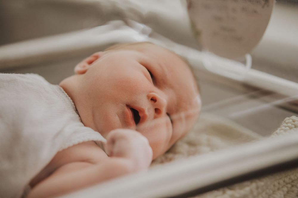 A peaceful sleeping newborn in soft white clothing rests in a hospital bassinet.