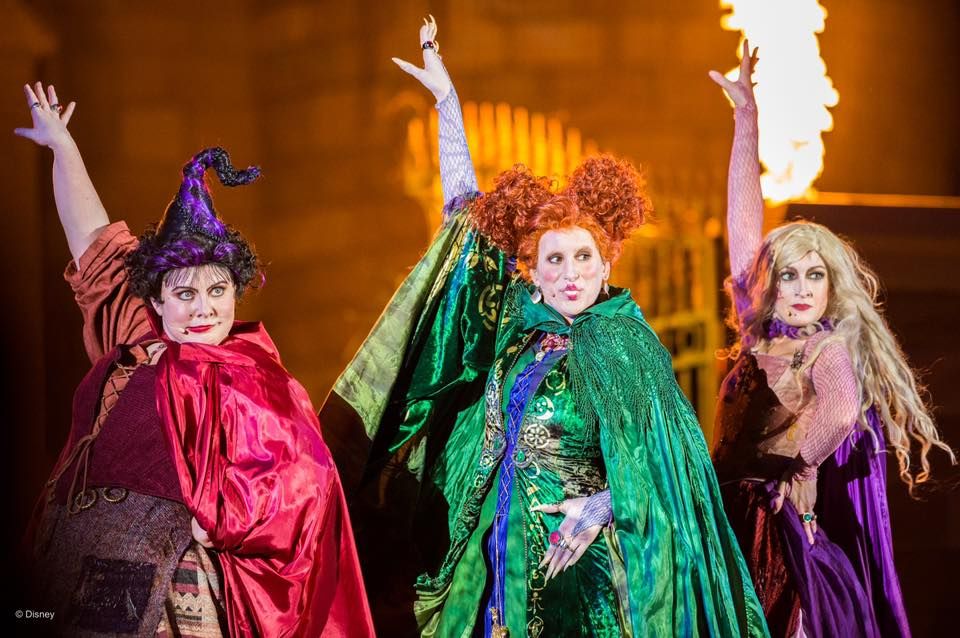 Three costumed performers in witch outfits perform during a Halloween-themed show.