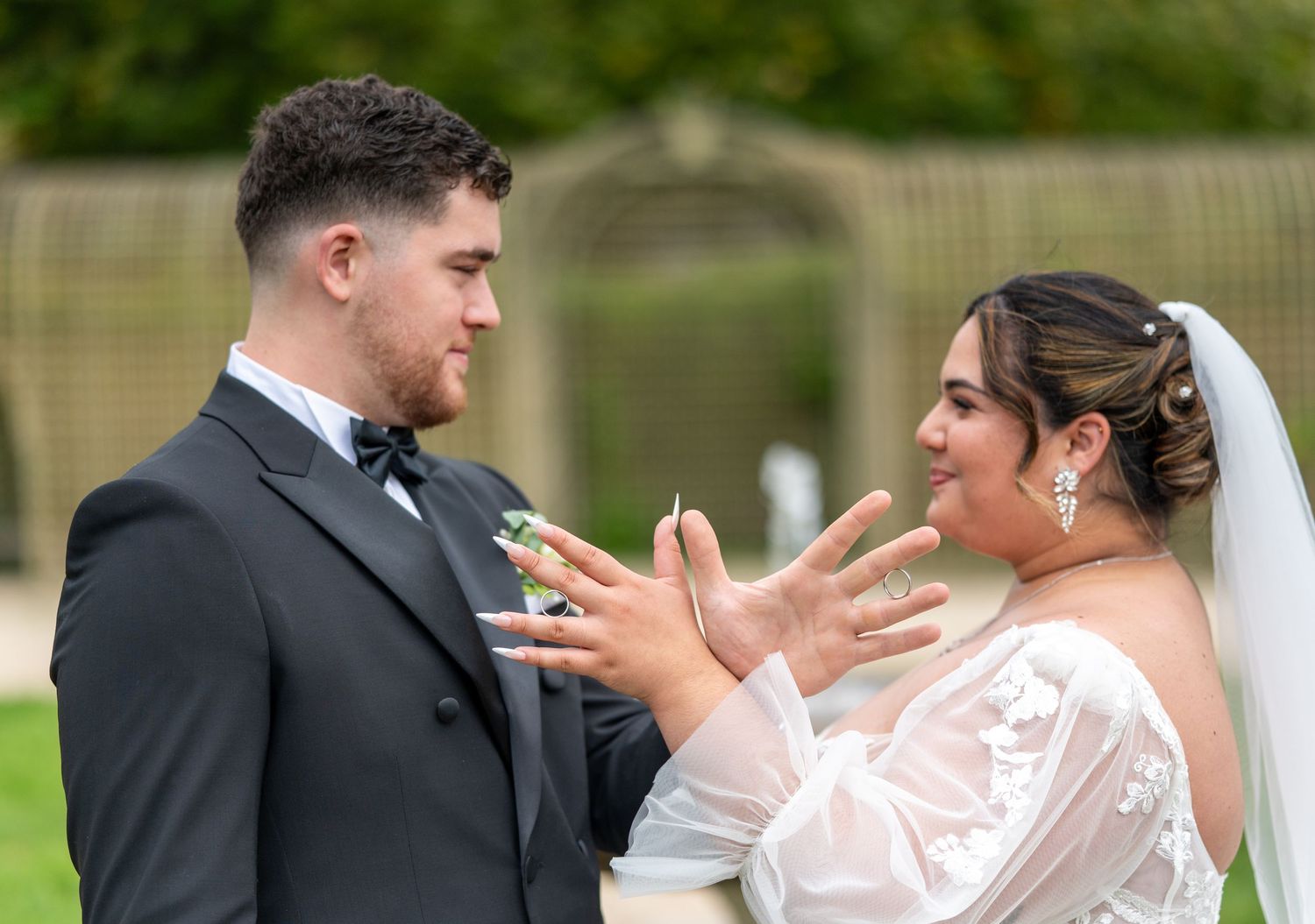 La mariée et le marié échangent des bagues à l'extérieur, portant une tenue de mariage, partageant un moment de joie le jour de leur mariage