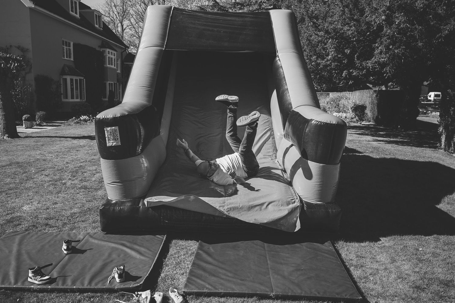 Person doing a backflip stunt on an inflatable bounce house in a backyard setting, captured in black and white.