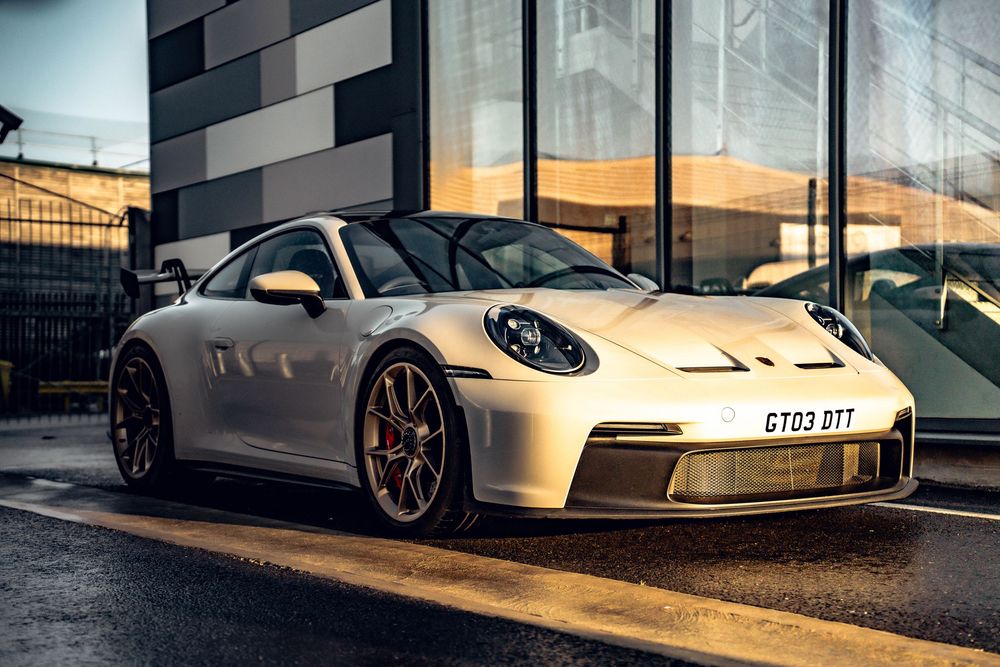 White Porsche 911 GT3 parked in front of modern building during sunset with reflective facade.