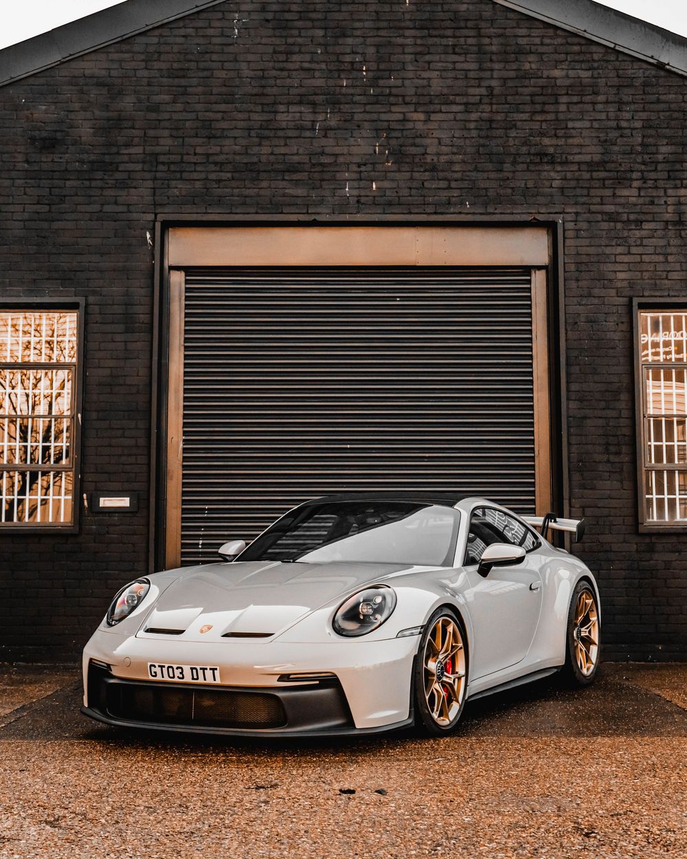White Porsche 911 GT3 parked in front of industrial brick building with roller door.