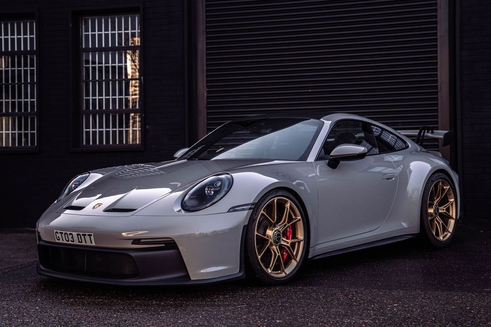 Silver Porsche 911 GT3 with prominent rear wing photographed against dark industrial backdrop.