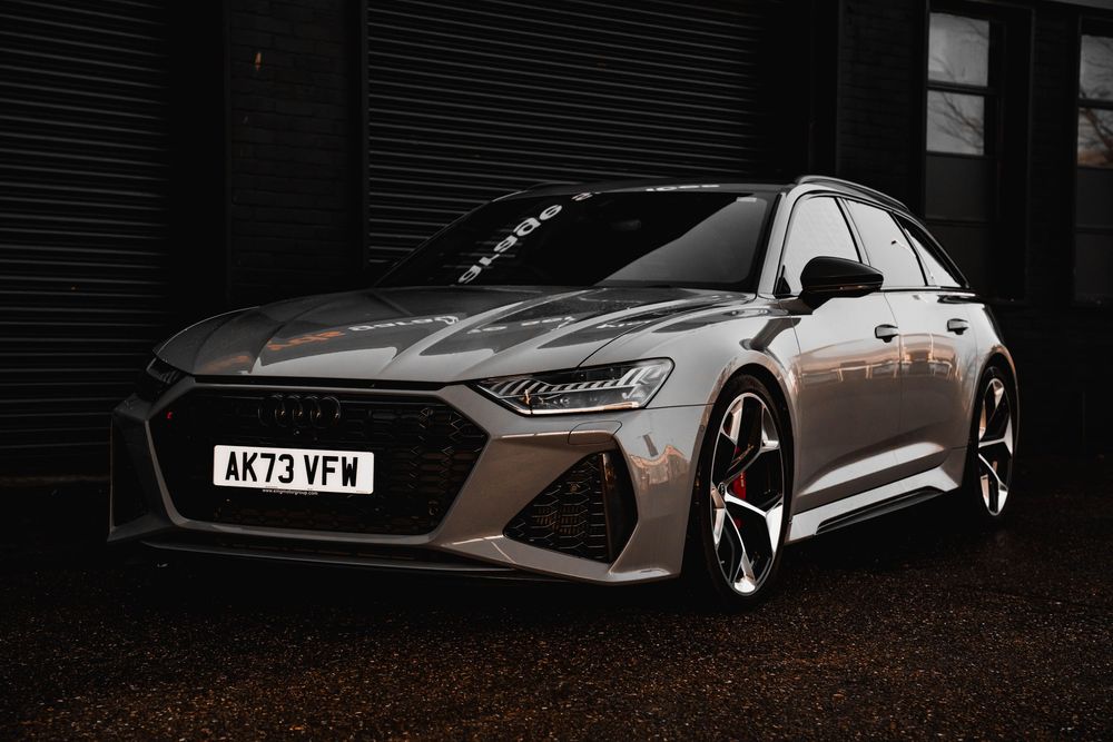 Bronze Audi RS6 front quarter view against dark industrial background.