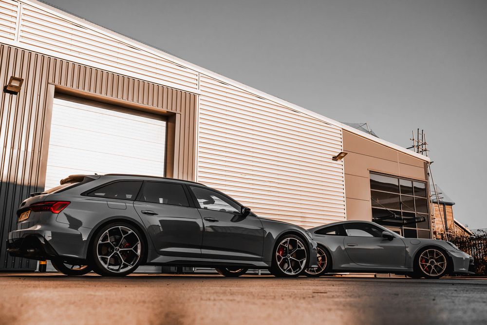 Two luxury performance cars in matte gray finish parked against an industrial building backdrop.
