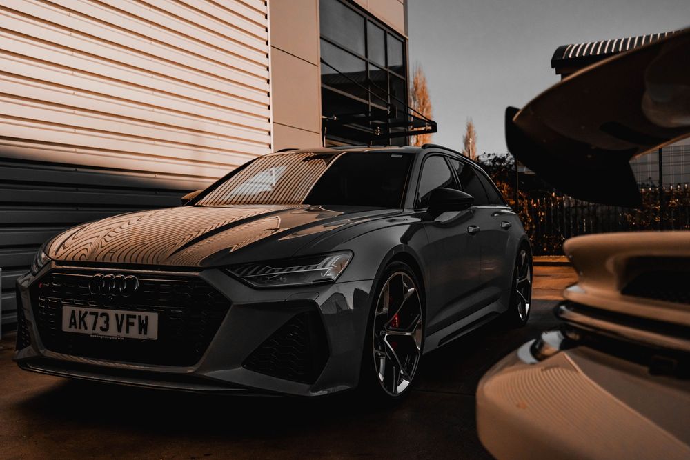 Matte black Audi RS6 Avant photographed at dusk against an industrial building.