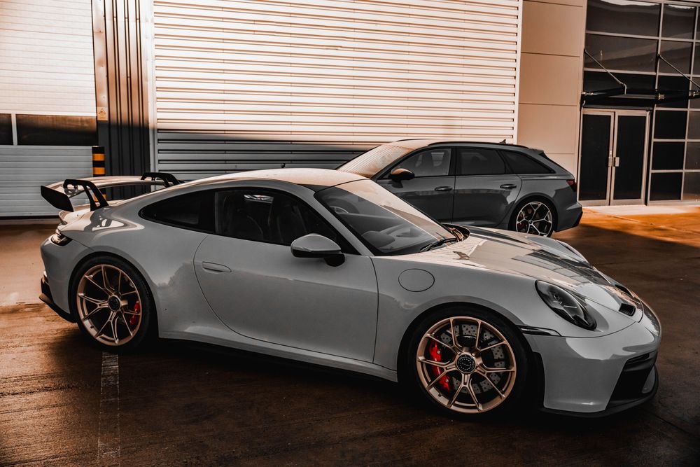 Silver Porsche 911 GT3 with prominent rear wing parked next to a dark wagon.