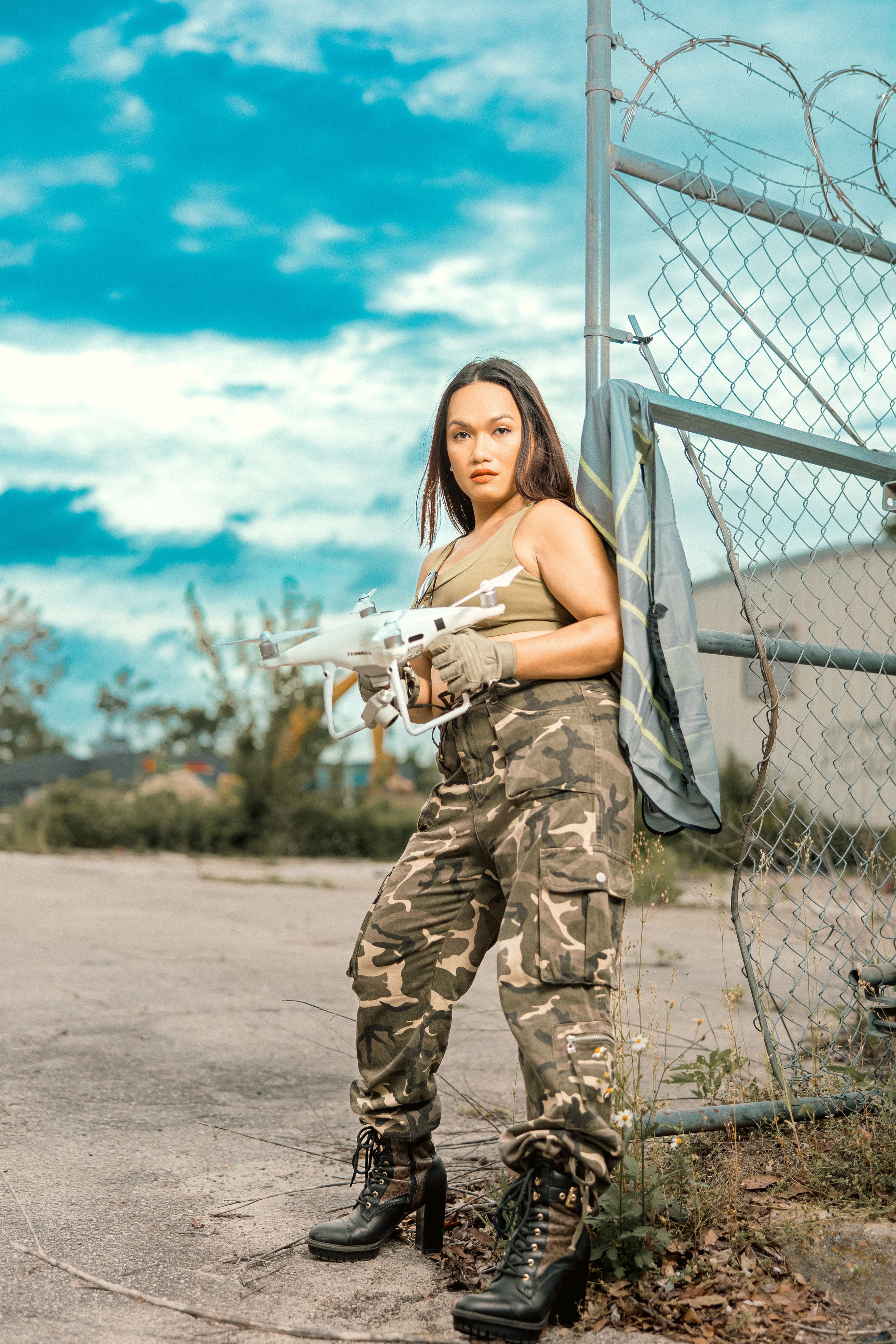 Industrial worker in camo pants poses near chain link fence on construction site.