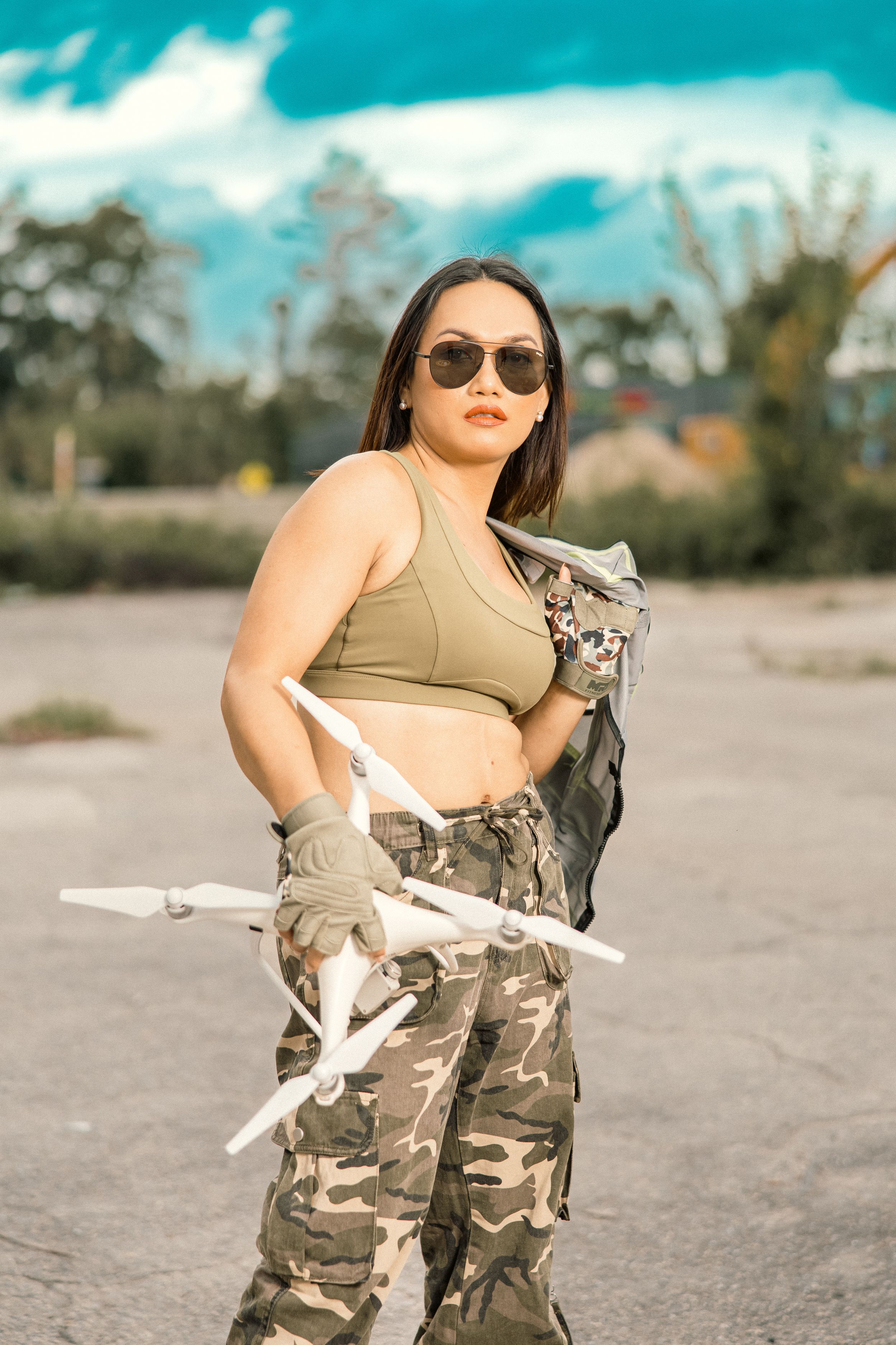 Outdoor photoshoot with camouflage pants and drone against bright blue sky.