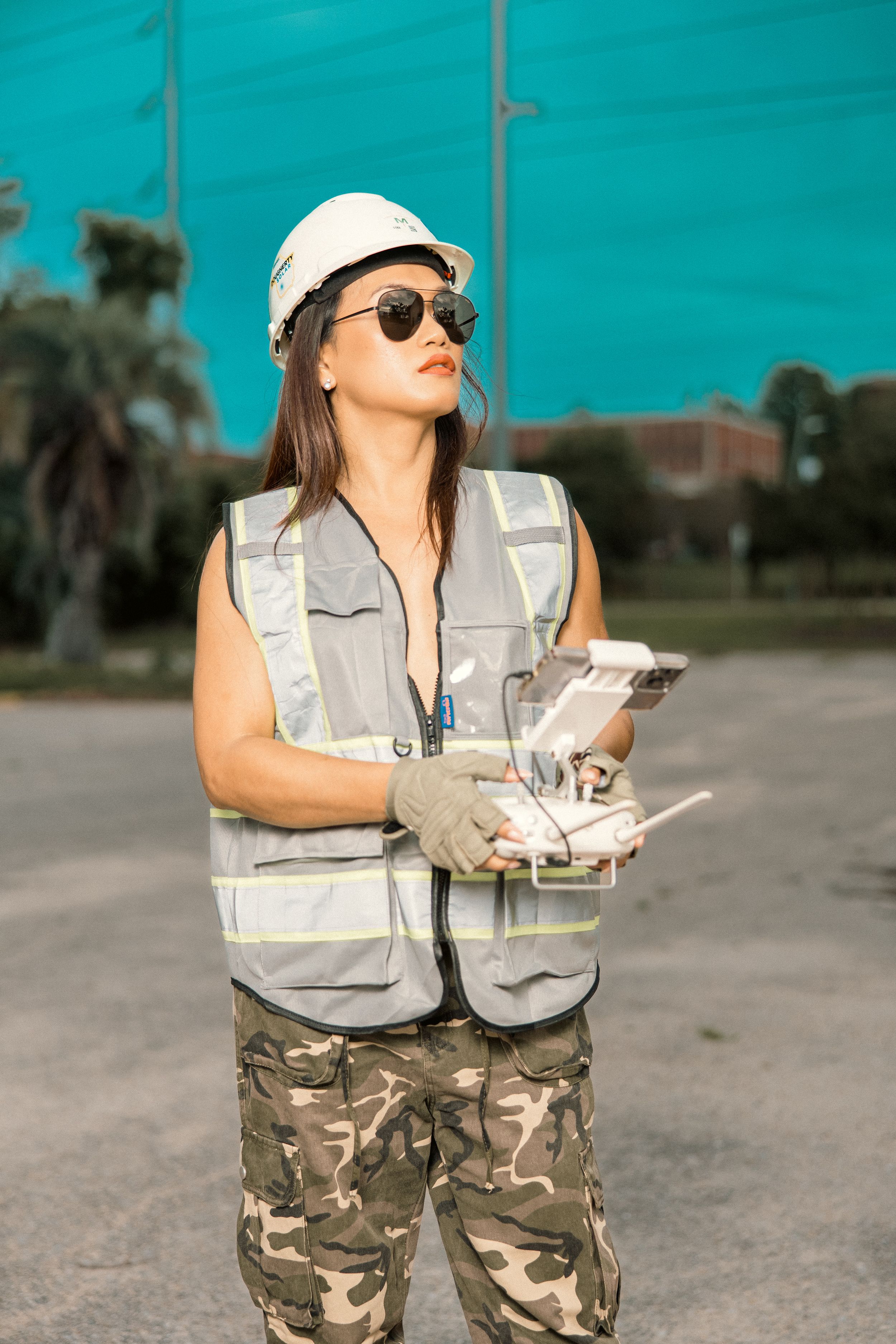 Professional in hard hat and safety vest operates drone controller in outdoor setting.