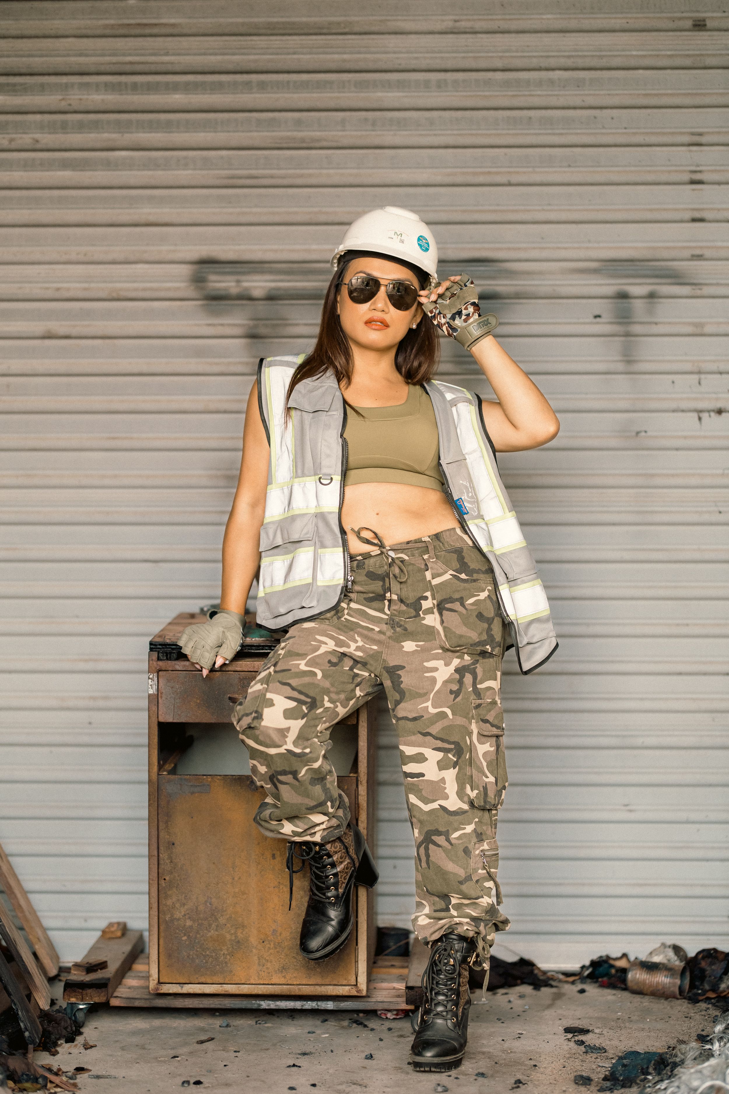 Industrial style portrait featuring worker in safety vest and combat boots against metal door.