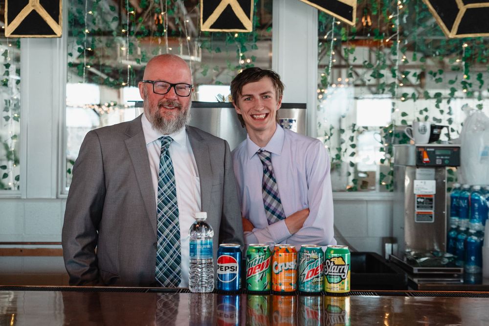 Two people in business attire stand at a bar counter with colorful canned beverages displayed in front of them.