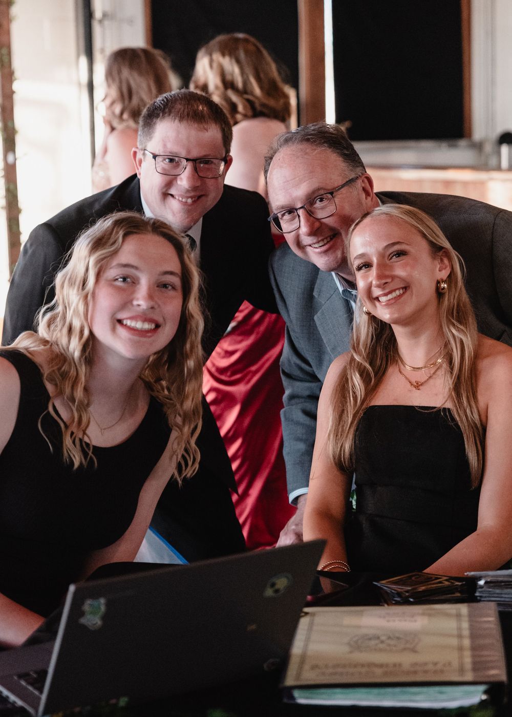 A group of people gathered around a laptop at a table indoors smiling at the camera.