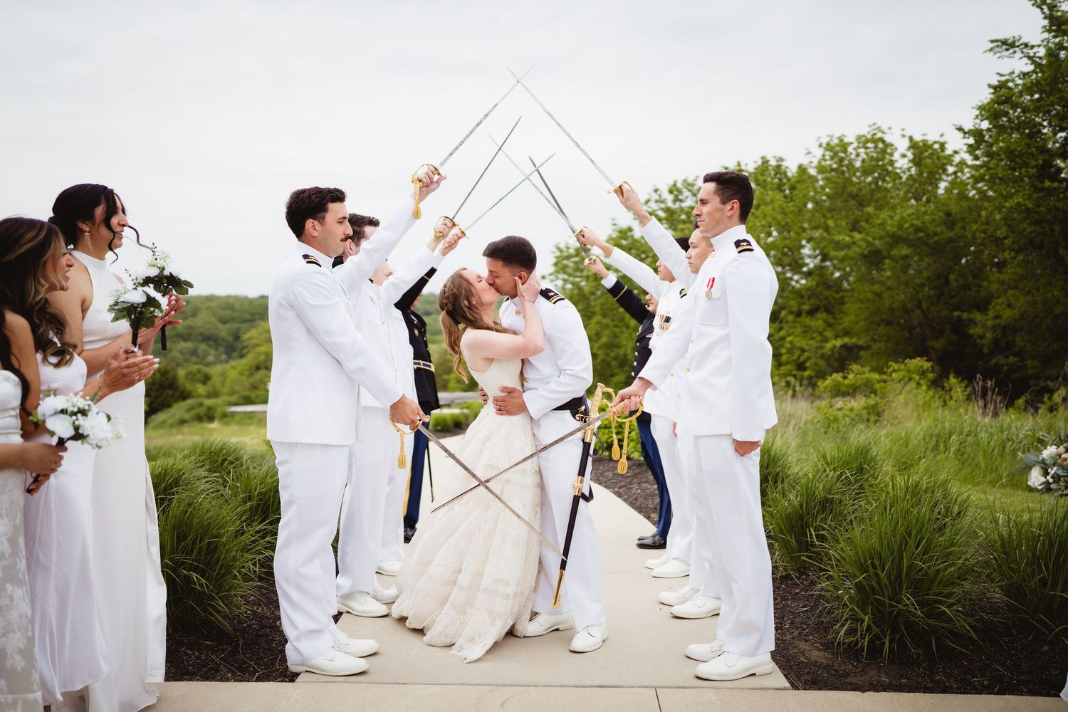 Wedding party in white attire poses for creative outdoor group photos in a grassy garden setting.