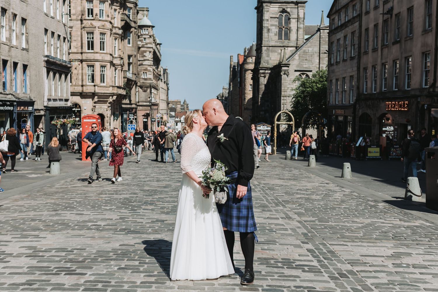 A lovely wedding couple share a romantic moment on Edinburgh's Royal Mile with historic architecture in the background.