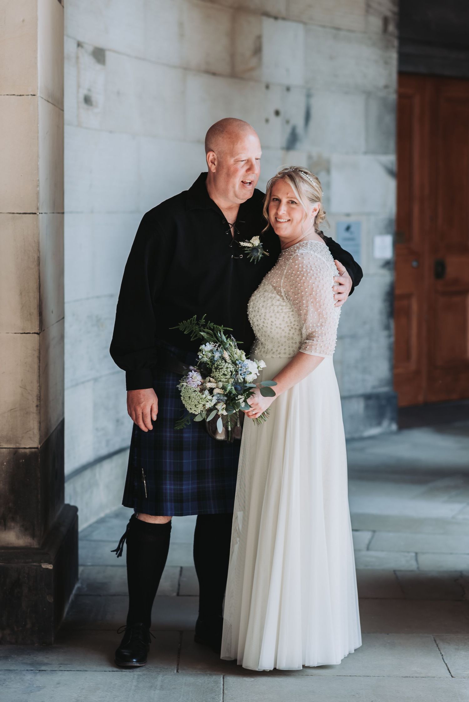 A tender moment captured between a couple in wedding attire against a stone wall backdrop.