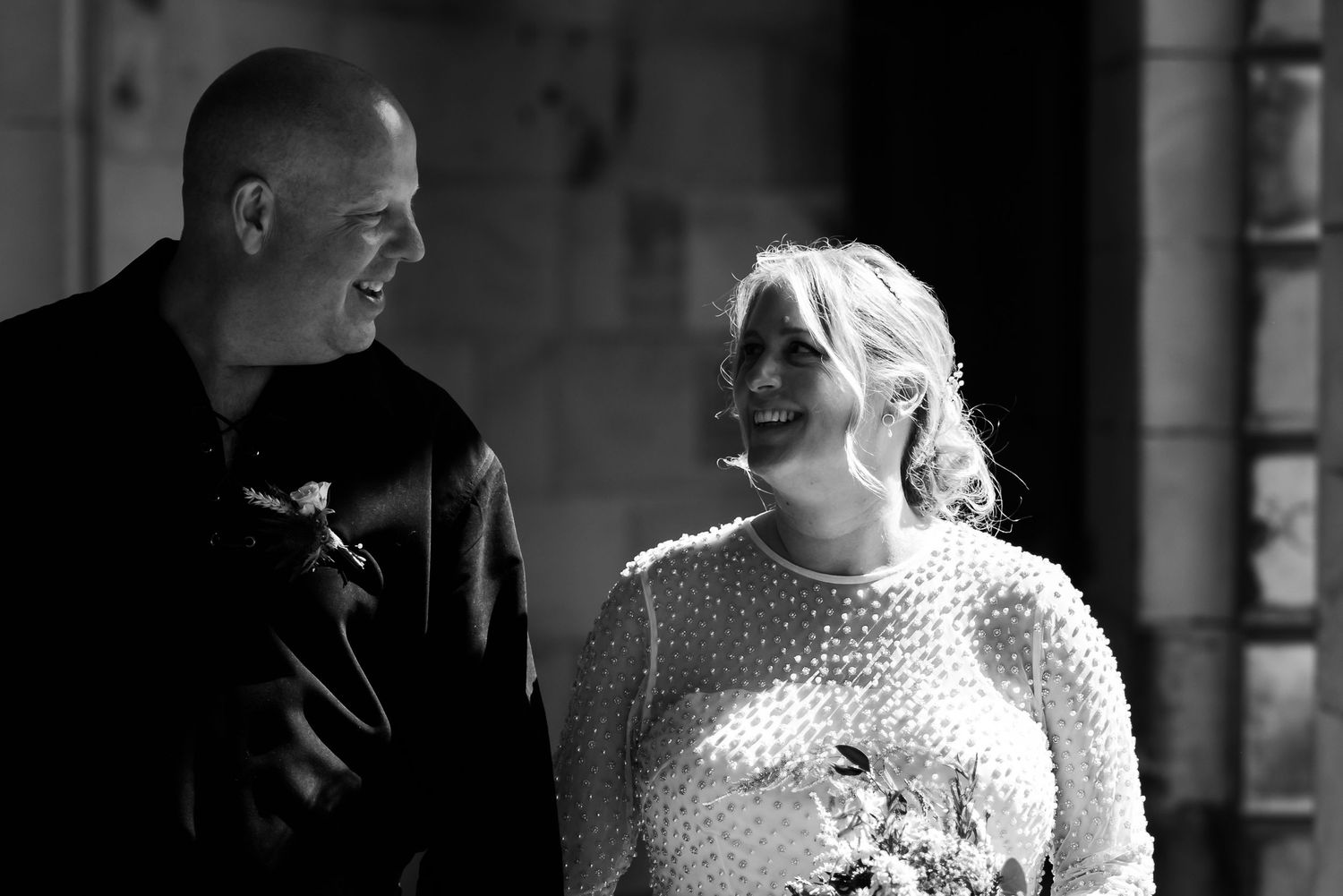 A black and white candid moment showing joyful laughter between a couple in wedding attire.