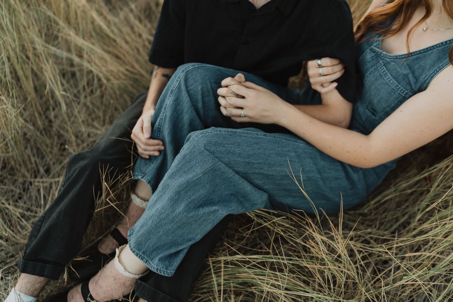 Intimate couple sitting close together in tall grass wearing casual denim.