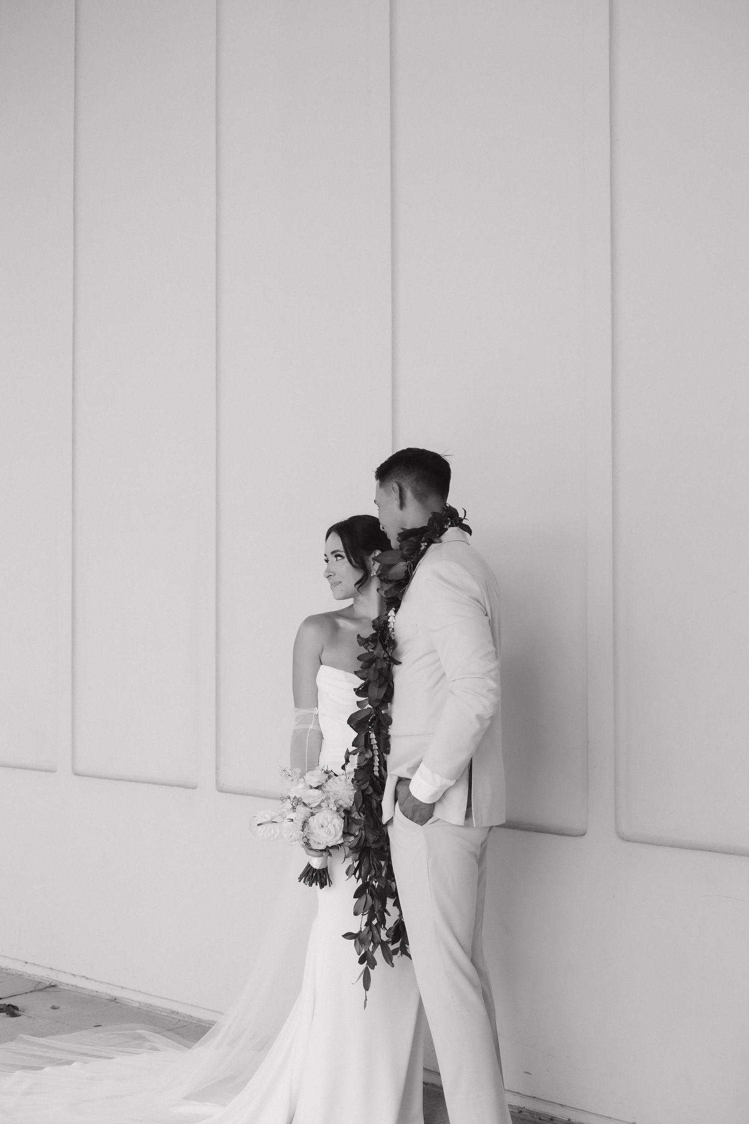A wedding couple poses against a white wall, black and white photo