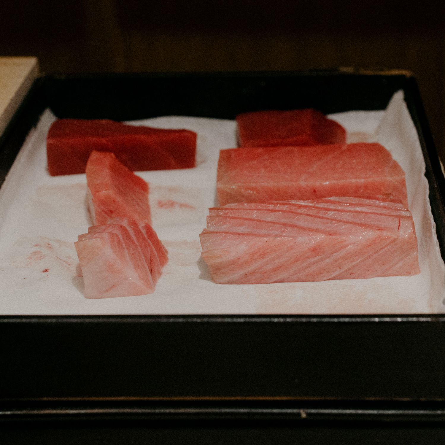 Fresh cuts of tuna arranged on a black serving tray with white paper.