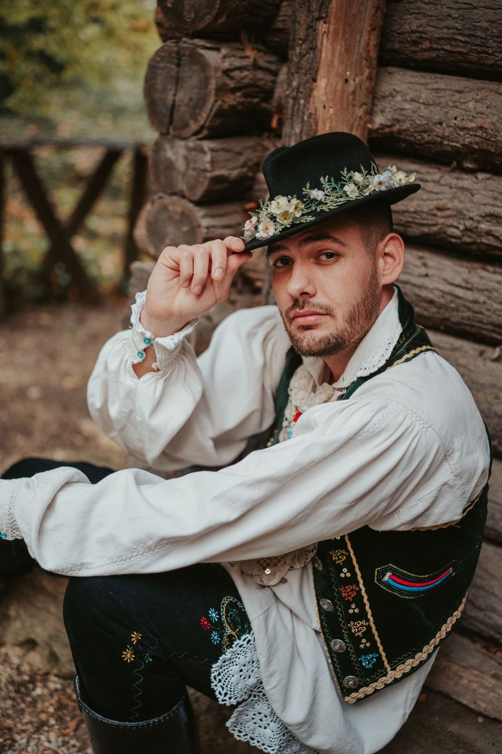 Traditional folk costume with embroidered vest and decorative hat against log cabin wall.