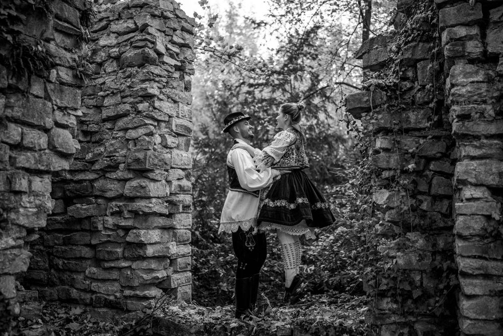 A black and white photo of a couple in traditional dress embracing between stone walls.