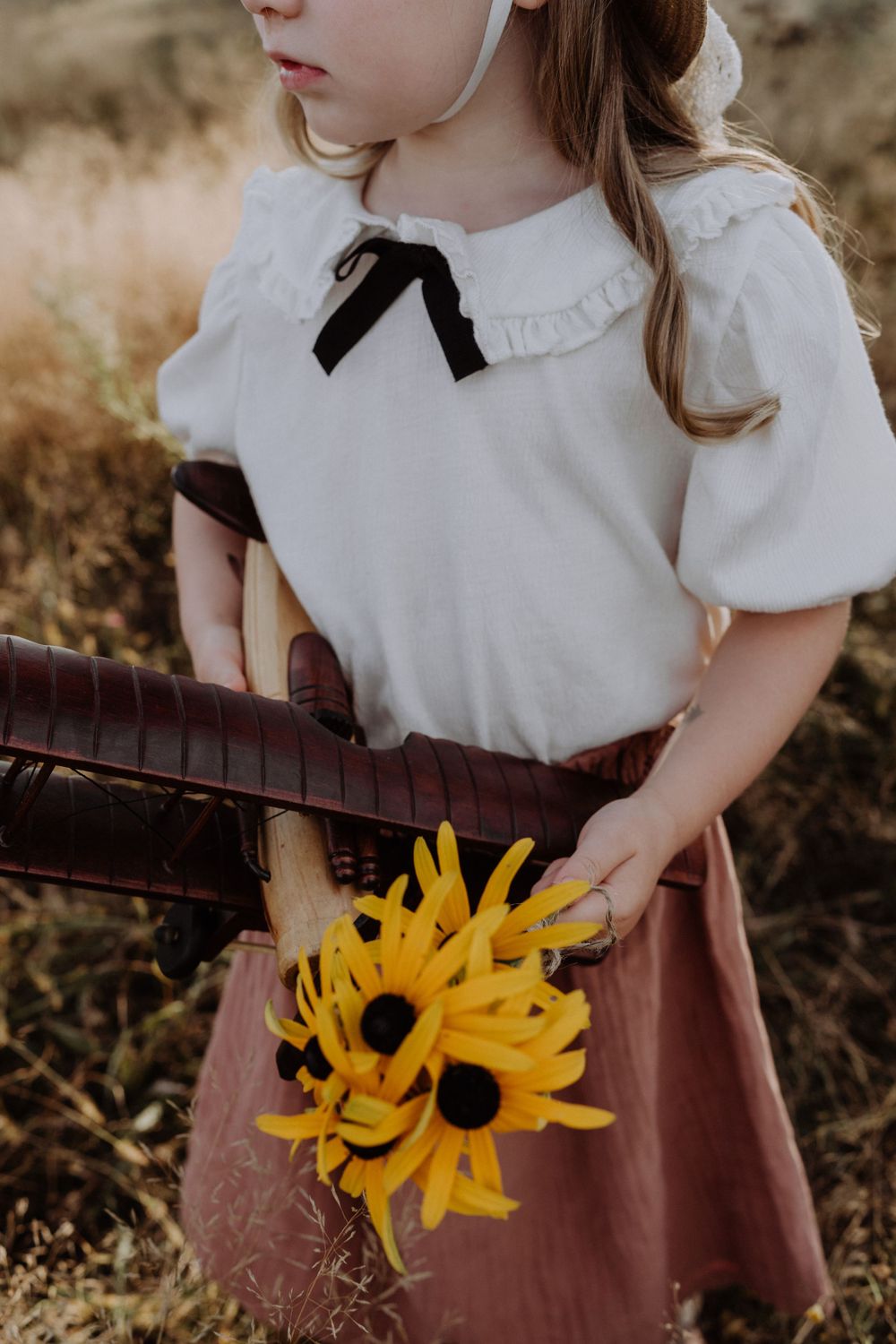 Vintage-inspired outfit detail with white blouse, black bow and yellow sunflowers against pink skirt.