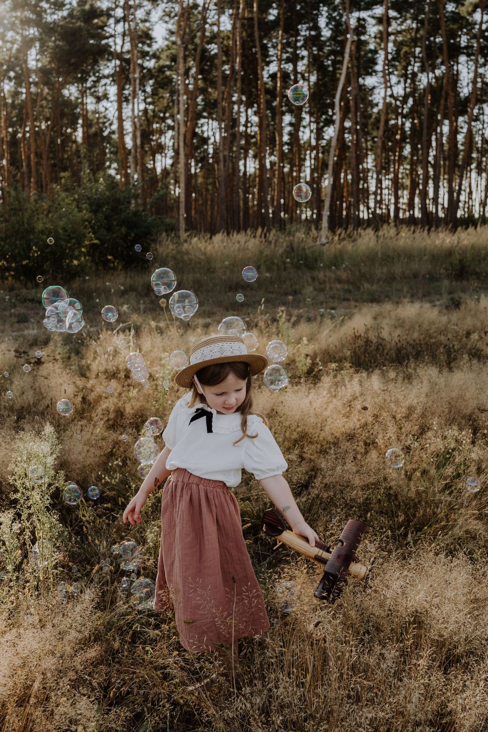 Whimsical outdoor scene with floating bubbles around figure in vintage dress and hat.
