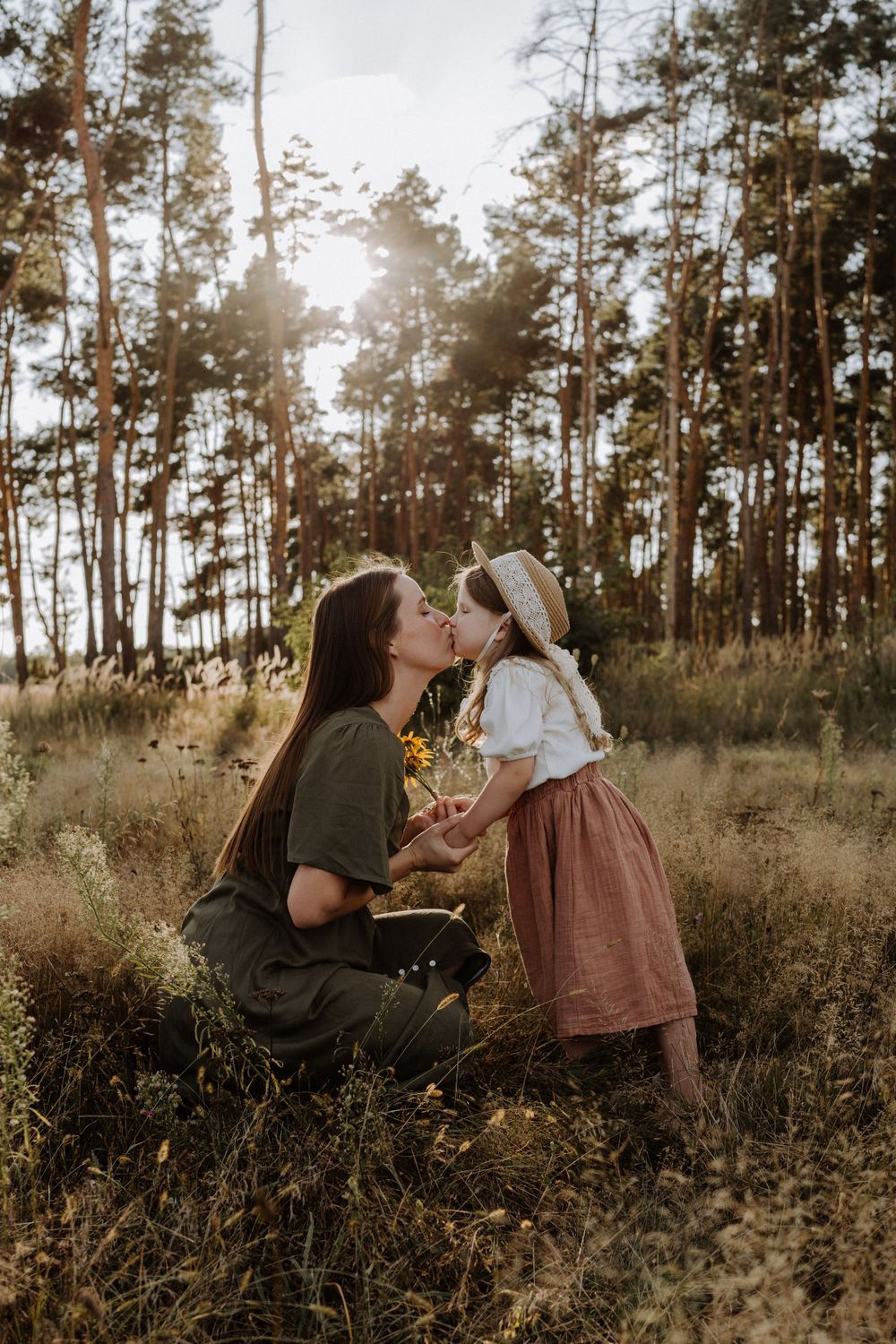 Tender moment captured in sunlit forest between parent and child in vintage-inspired outfits.