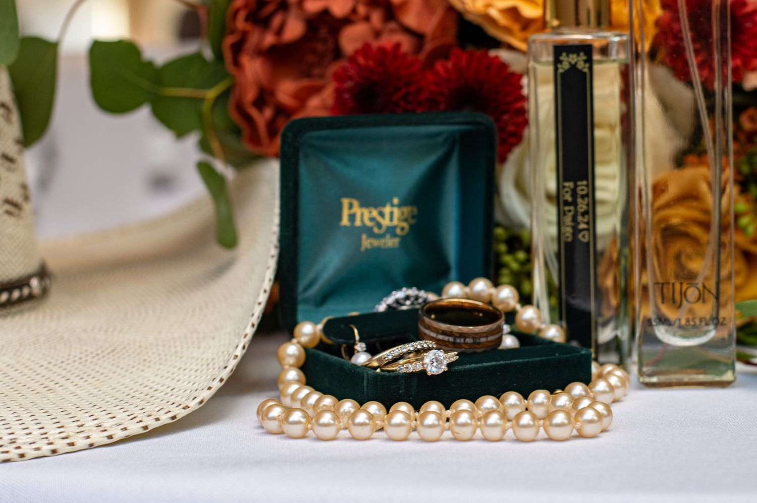 Wedding rings and pearl necklaces were arranged with perfume bottles on white tablecloth.