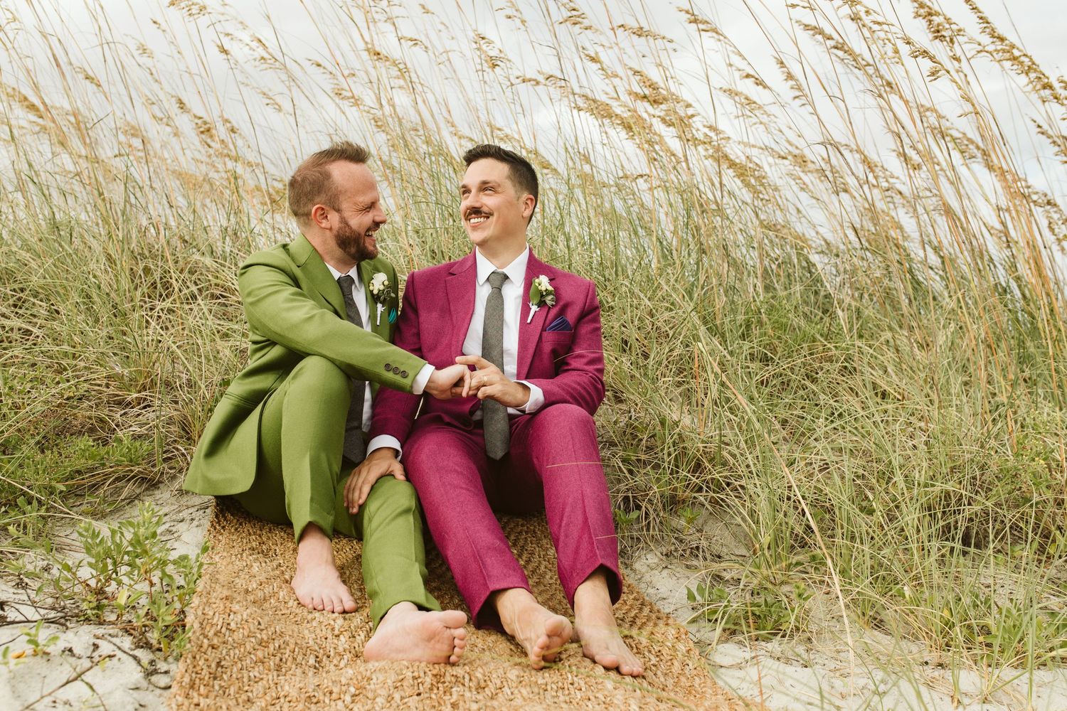 Two people in colorful suits sitting on beach grass and sharing a joyful moment together.
