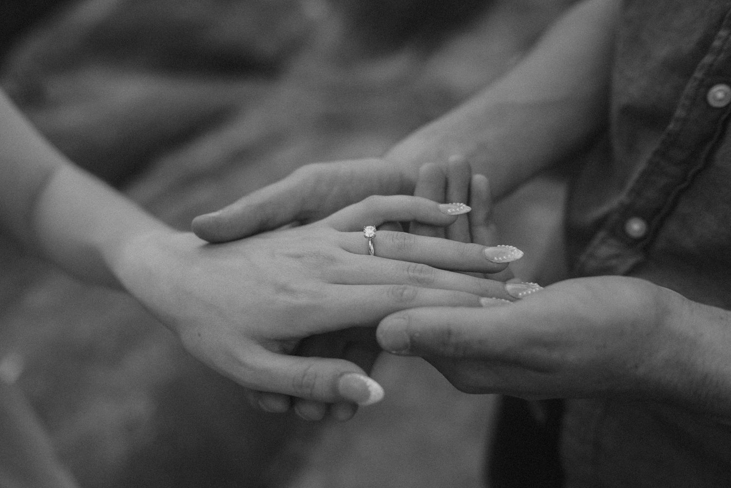 A man holds his fiancé's hand while showing off her engagement ring